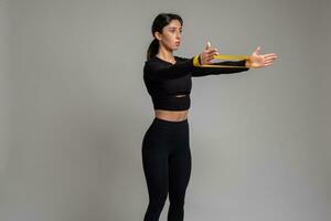 Girl doing arm and shoulder exercises with resistance band on grey background photo