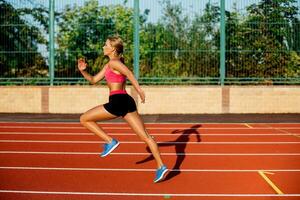 lado ver hermosa joven mujer ejercicio trotar y corriendo en atlético pista en estadio foto