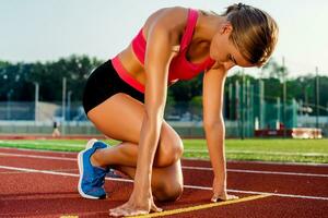 Young woman athlete at starting position ready to start a race on racetrack. photo