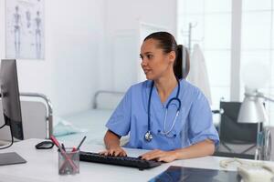 Medical practitioner using computer in hospital office. Health care physician using computer in modern clinic looking at monitor, medicine, profession, scrubs. photo