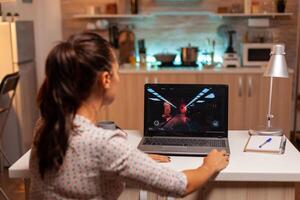 Female game developer working on new project on personal laptop in home kitchen during night time. Professional gamer playing online videop games on her personal computer. Geek cyber esport. photo