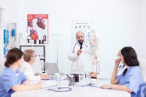 Expert radiologist demonstrating on skeleton during briefing with medical staff in hospital meeting room. Clinic therapist talking with colleagues about disease, medicine professional photo