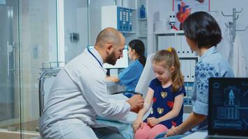 Medical practitioner bandaging child injured arm sitting in bed. Healthcare physician specialist in medicine providing health care service radiographic treatment examination in hospital cabinet. photo