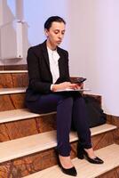 Exhausted tired businesswoman working on project deadline using smartphone. Serious entrepreneur working on job project sitting on staircase of business building at night hours for job. photo