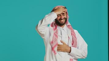 Cheerful person laughing at a joke in studio, having fun while he wears muslim traditional clothing and kufiyah. Young arab man enjoying laugh with people, expressing happiness and joy. photo