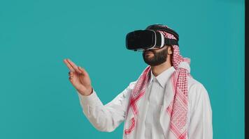 Middle eastern man using vr headset in studio, enjoying shoot with virtual reality technology on interactive glasses. Young person aving fun with 3d simulation, modern hobby and gadgets. photo