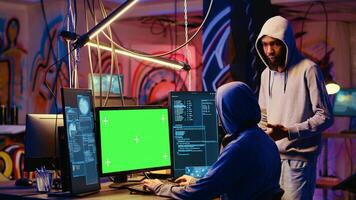 Hacker using green screen PC to do data breaches and financial theft in graffiti painted hideout. Rogue programmers using chroma key monitor for stealing users bank account credentials photo