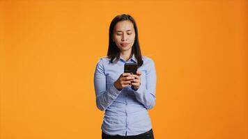 Young person texting messages on mobile device in studio, browsing through social media app and talking to friends online. Modern smiling woman using sms and texts for communication. photo