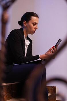 Overworked businesswoman smiling during video call about project deadline. Entrepreneur talking with client using smartphone for video call sitting on stairs. photo