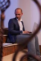 Tired stressed businessman lose concentration on business deadline at workplace. Corporate entrepreneur using laptop doing overtime sitting on stairwell. photo