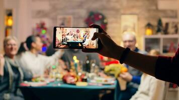 Girl taking a family portrait with her phones while celebrating christmas. Traditional festive christmas dinner in multigenerational family. Enjoying xmas meal feast in decorated room. Big family reunion photo