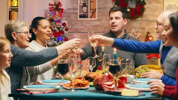 Family with different ages clinking glasses with champagne celebrating christmas. Traditional festive christmas dinner in multigenerational family. Enjoying xmas meal feast in decorated room. Big family reunion photo