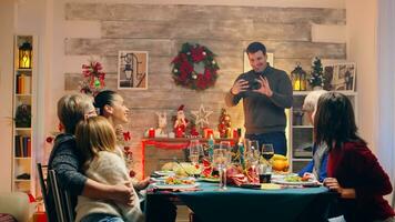 Adult man taking a photo with the family at christmas reunion. Happy family. Winter holidays. Traditional festive christmas dinner in multigenerational family. Enjoying xmas meal feast in decorated room. Big family reunion