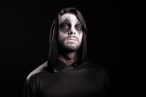 Man with creepy face dressed up like grim reaper over black background. photo