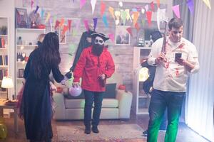 Young man dressed up like a zombie with an axe scrolling on his phone at halloween party. photo