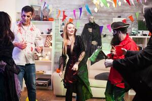 Beautiful woman dressed up like a vampire dancing with a pirate while holding his axe at halloween celebration. photo