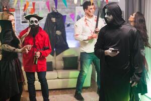 Bored man dressed up like a grim reaper at halloween party using his phone. photo