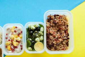 Various of healthy lunch boxes over yellow and blue background. Take away of natural organic fitness nutrition for diet. Top view, flat lay. Packed daily meals. photo