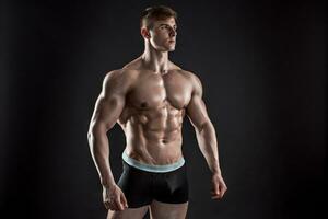 Muscular bodybuilder guy doing posing over black background photo