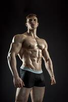 Muscular bodybuilder guy doing posing over black background photo