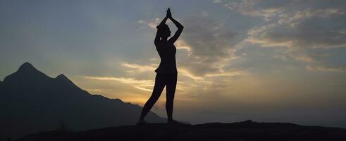 ai generado silueta de un mujer practicando yoga en el cumbre con montaña antecedentes. ai generado foto