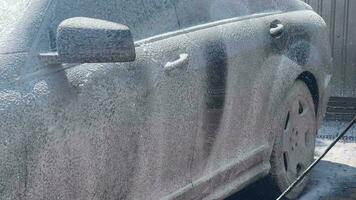 Foam coating of a car with a high-pressure washer. Open car wash. The process of applying soap suds to the sides of a car using a pressure washer - close-up with selective focus. video