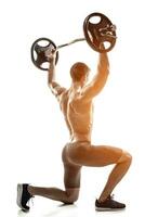 Fitness man standing on knee and holding barbell, rear view photo