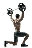 Fitness man standing on knee and holding barbell, rear view photo