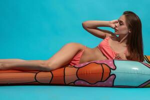 Slim girl in swimsuit lying on inflatable mattress on blue background photo