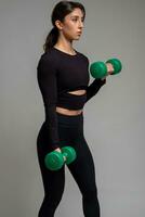 Fit brunette doing dumbbell bicep curl on grey background photo