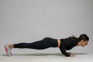 Woman in black sportswear doing push-ups on grey background photo