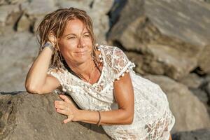 beautiful blond woman wearing a white shirt posing on a rock photo