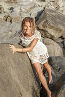 beautiful blond woman wearing a white shirt posing on a rock photo