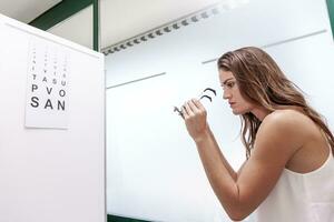 beautiful woman testing new auxiliary lenses with phoropter during an eye examination photo