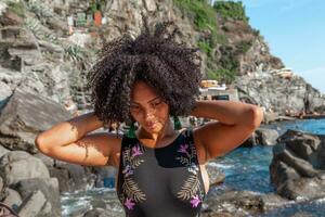 portrait of a pretty curly Venezuelan woman relaxing on a rock in the sea photo