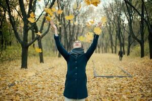 Woman throwing yellow leaves in air photo