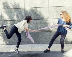 two pretty girls improvise a tug of war with a scarf photo