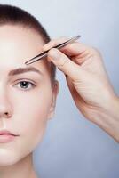 Young woman with short hair plucking eyebrows tweezers close up photo