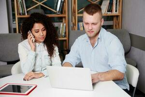 Two Serious Young Business People Sitting Table with Laptop photo