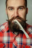 young man comb his beard and moustache  gray background photo