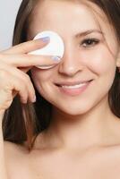 Happy smiling beautiful young woman cleaning skin by cotton pad. photo