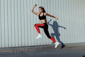 Full length of healthy female exercising and jumping outdoors. photo