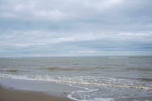 Dunes, clouds, breakwater at ebb tide on sandy beach photo