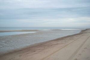 Dunes, clouds, breakwater at ebb tide on sandy beach photo