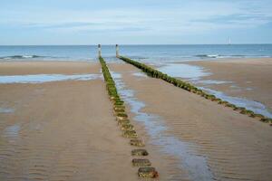 Dunes, clouds, breakwater at ebb tide on sandy beach photo