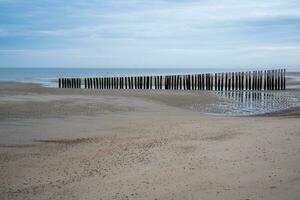 Dunes, clouds, breakwater at ebb tide on sandy beach photo