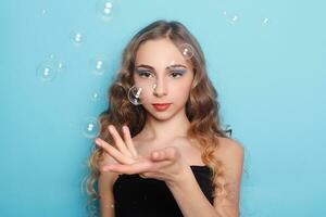 Beautiful young woman with soap bubbles over cyan background photo