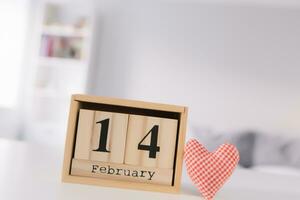 Valentines day concept. Hand make yarn red heart beside wooden block calendar set on Valentines date 14 February on table and bright room background. Happy valentine day. photo