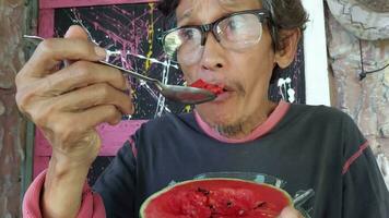 An elderly man eats a very red watermelon. He looks delicious and refreshing. He is happy with his eating. video