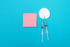 Vaccination, Immunology or Revaccination Concept Two Medical Disposable Syringe Lying on Blue Table in Doctor's Office in a Hospital or Clinic. Blank Pink Sticky Note Mock Up with Copy Space photo